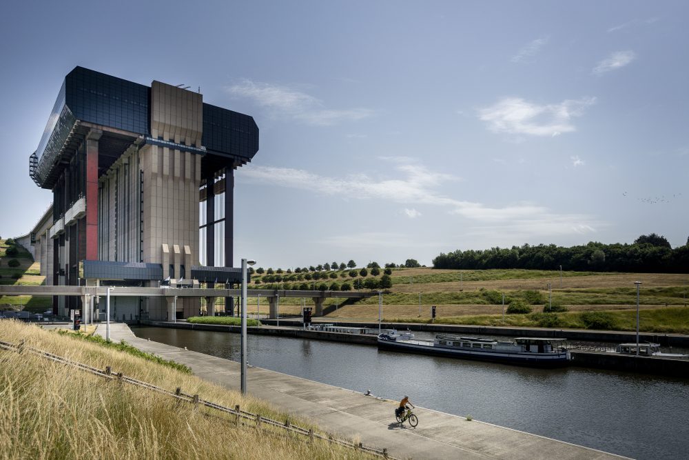A cyclist rides along a canal near the impressive Strépy-Thieu boat lift under a clear sky.