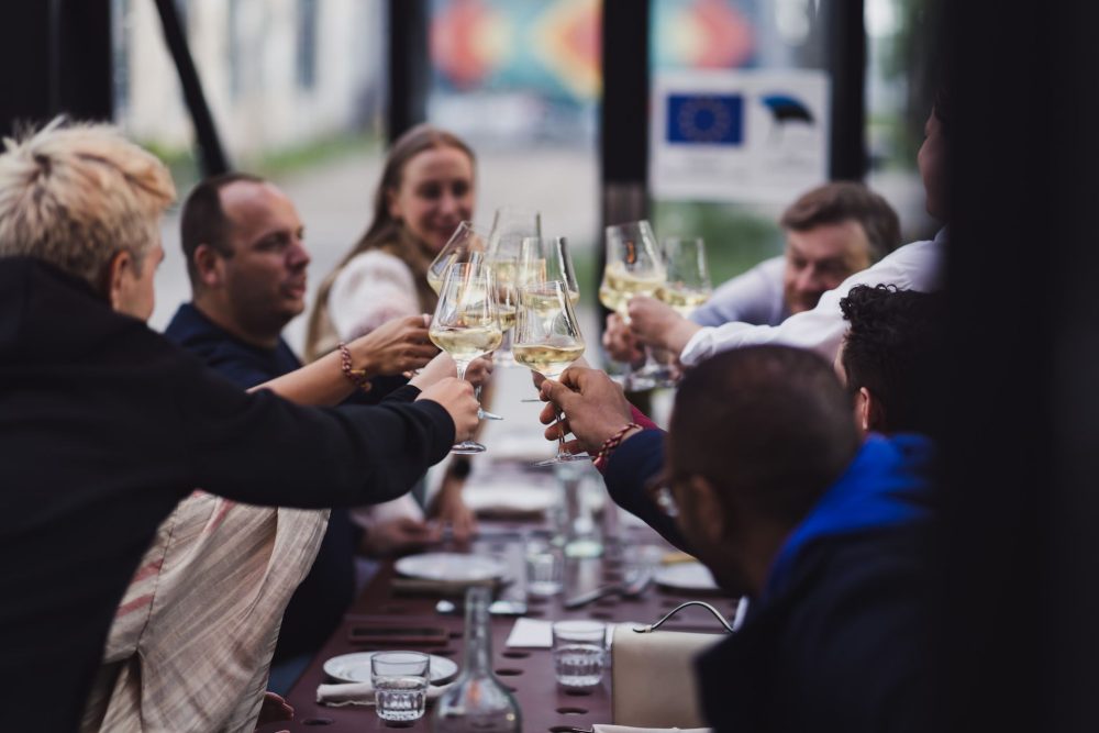 Group of friends toasting Estonian white wine at a long outdoor table in Tallinn.