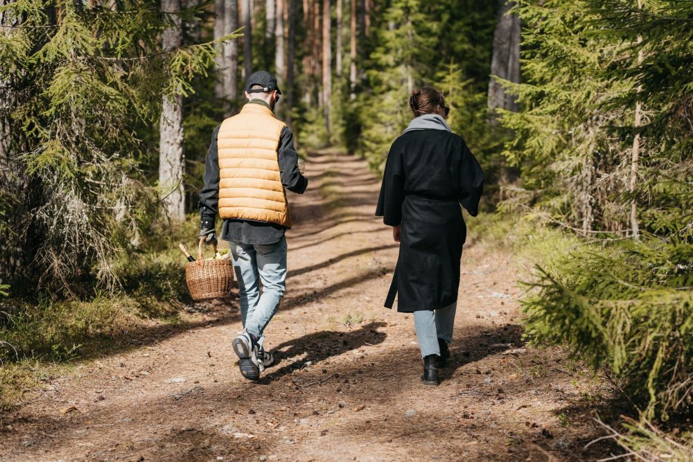 Couple walking through a pine forest trail with a picnic basket of Estonian wine.