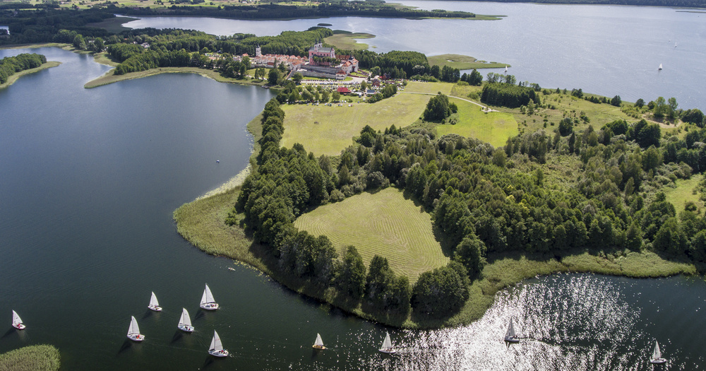 Aerial view of a serene lake surrounded by lush greenery, with a charming village and sailboats gliding across the water.