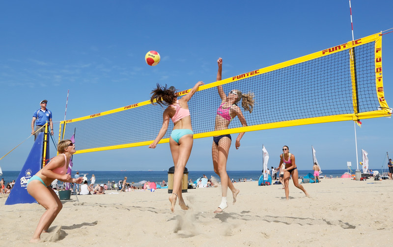 Women playing an energetic game of beach volleyball on a sandy beach with a clear blue sky in Scheveningen, Netherlands.