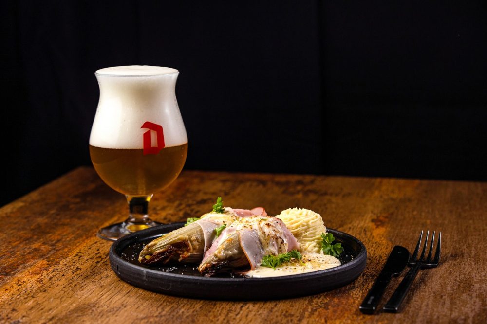 A plate of gourmet seafood wrapped in ham, accompanied by creamy mashed potatoes and a glass of beer on a wooden table.