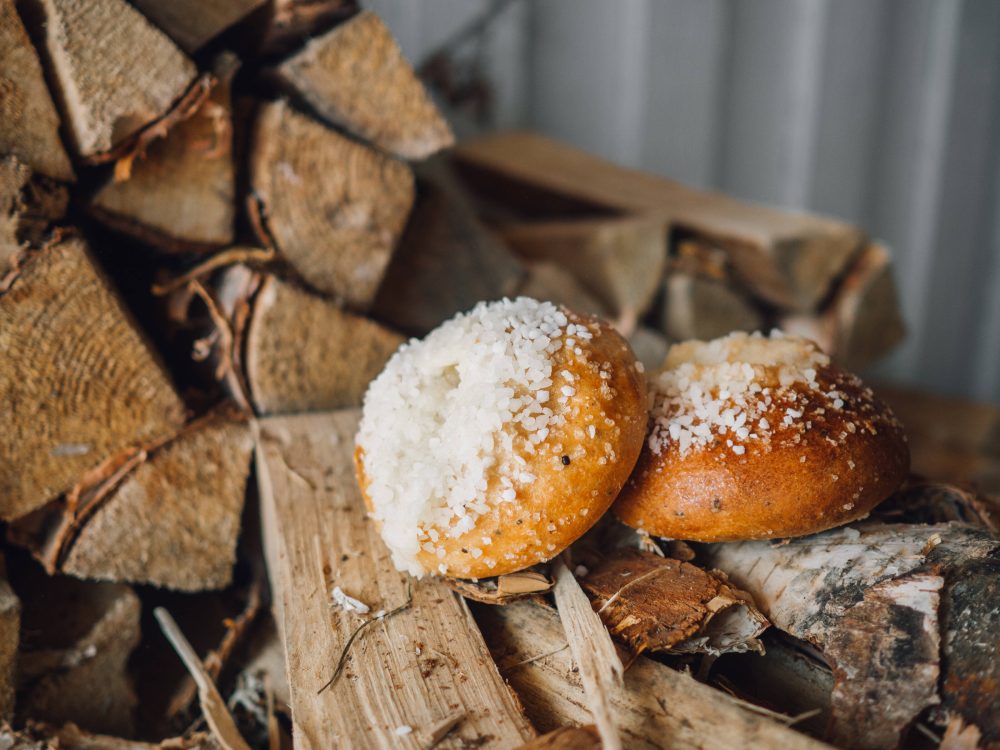 Two golden, soft pastries topped with coarse white sugar sit on wooden logs and rustic foliage.