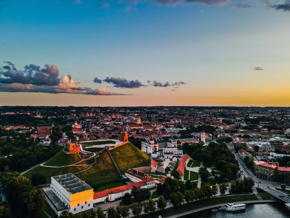 Panoramic view of a Vilnius old town with colourful buildings, a tall church tower, an ornate orthodox cathedral, and modern cityscape in the background.