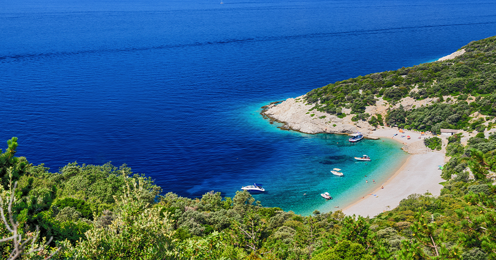 Secluded cove with crystal-clear water and boats anchored by the shore.