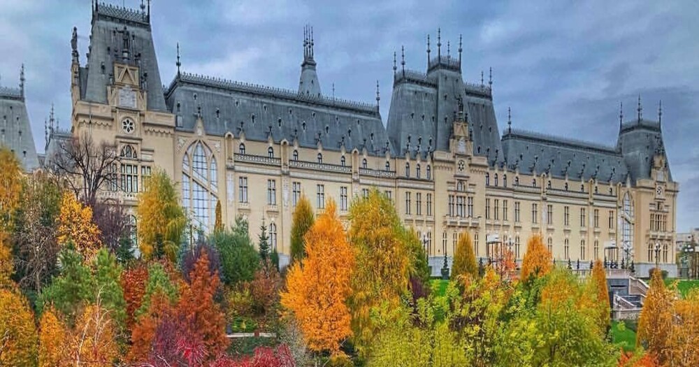A grand historic building with a symmetrical façade, surrounded by vibrant autumn foliage under a cloudy sky.
