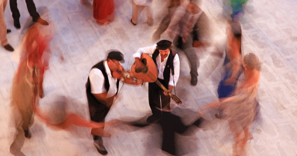 Delight in the sound and energy of music and dancing at Imerovigli, Santorini during a folklore festival.