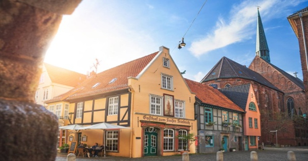 Charming historic buildings with colorful facades and a tall church spire under a bright blue sky in a quaint town square.