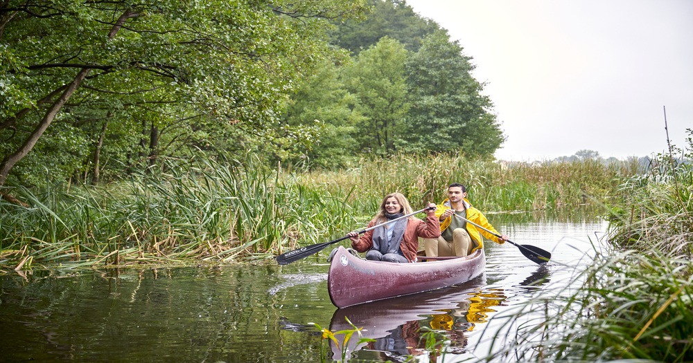 Couple canoeing through a narrow waterway surrounded by lush greenery in Mecklenburg-Vorpommern, Germany.