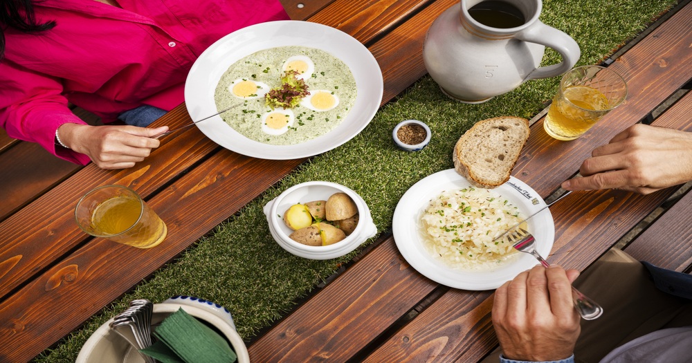 Traditional German cuisine served outdoors with creamy soup, boiled potatoes, sauerkraut, bread and beer on a wooden table.