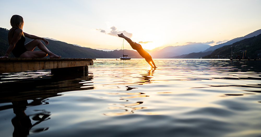 Man diving into a lake at sunset with mountains in the distance.