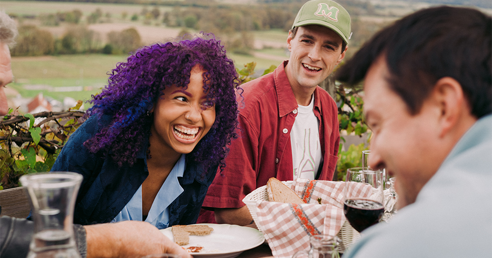 Friends sharing bread, wine, and laughter at a traditional Austrian wine tavern with vineyard views.