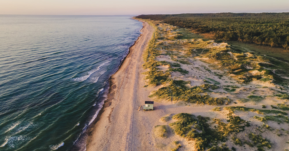 Remote view of Tisvilde Beach, Denmark, with sandy dunes and a small hut along the coast.