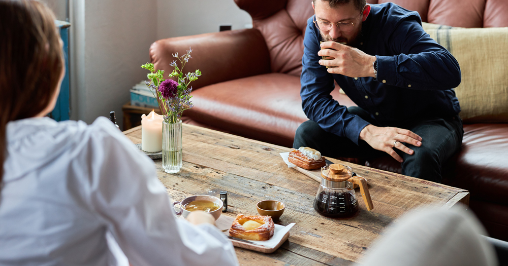 Couple enjoying coffee and Danish pastries in a relaxed café setting with rustic wooden table and natural light.