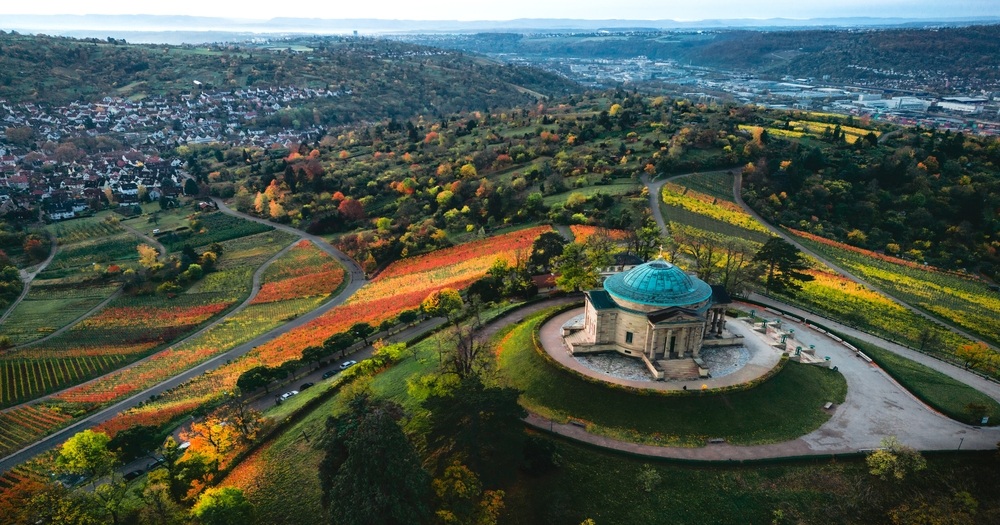 Aerial view of a scenic landscape featuring vibrant autumn vineyards, a historic gazebo, and a charming town in the distance.