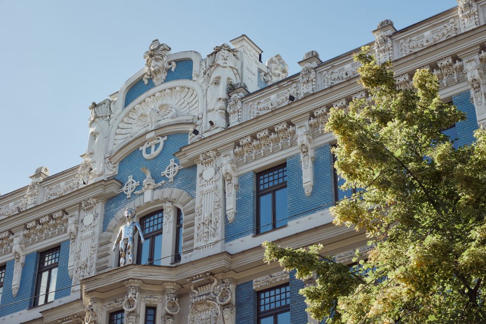 Close-up of an ornate Art Nouveau building facade in Riga, Latvia, featuring intricate sculptures and blue brickwork under a clear sky.