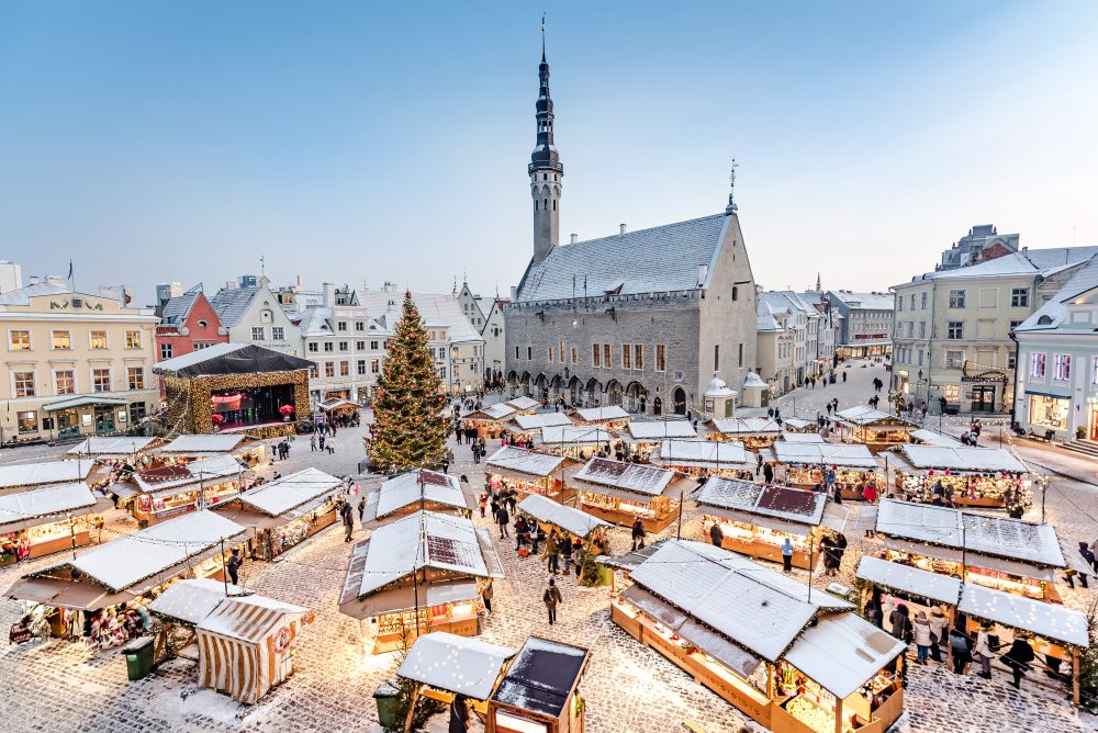Tallinn Christmas Market in Town Hall Square, Estonia, with snow-covered stalls, festive lights, a decorated Christmas tree, and the historic Town Hall tower in winter.