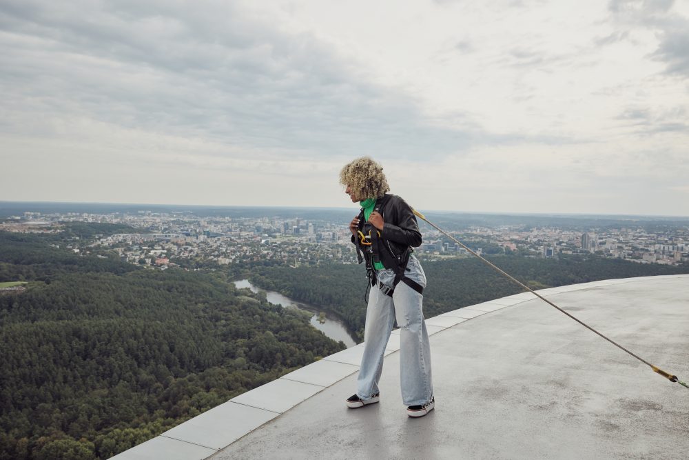 Woman harnessed on the edge of the Vilnius TV Tower, enjoying panoramic views of the city and surrounding forests.