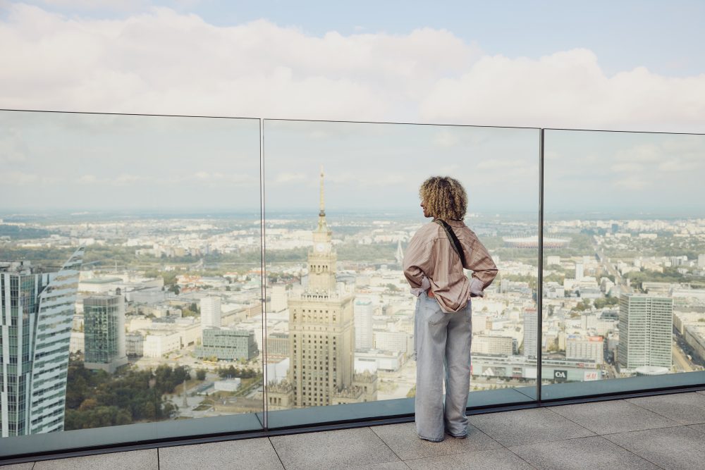 Panoramic view of Warsaw from a rooftop terrace, featuring the Palace of Culture and Science in the foreground.