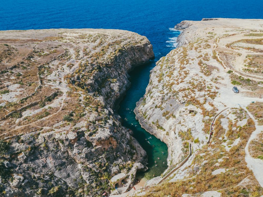 Scenic aerial shot of Wied il-Għasri, a narrow and secluded sea inlet flanked by rugged cliffs on Gozo, Malta.