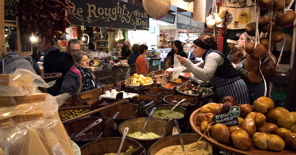 A bustling market scene filled with colorful produce, spices, and jars, as shoppers and vendors interact amidst vibrant displays.