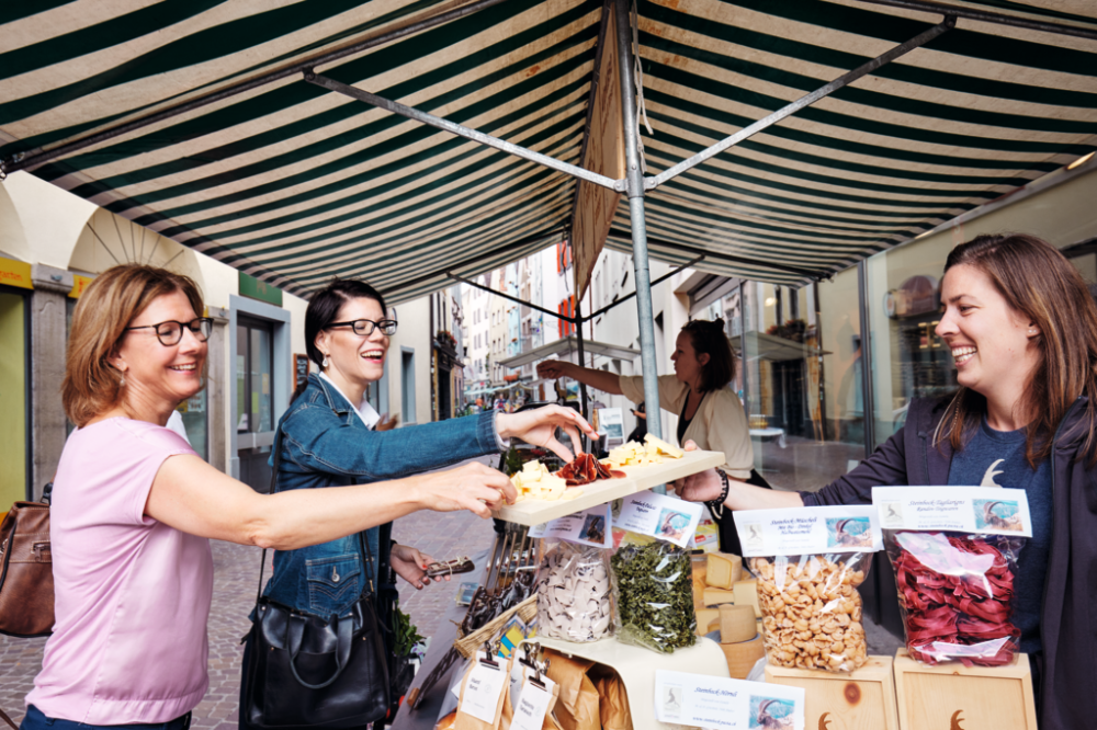 Two women sampling traditional Swiss delicacies at a stall in Chur Market.